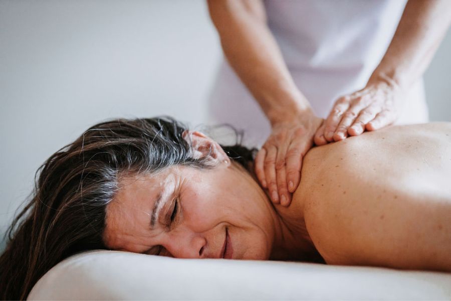 Eine Frau liegt auf einer Massageliege und sieht sichtlich entspannt aus. Sie bekommt eine Rebalancing-Nackenmassage und genießt die Berührung.